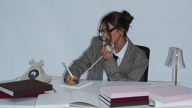 Person sitting at a desk with books and a lamp in a minimalistic room.